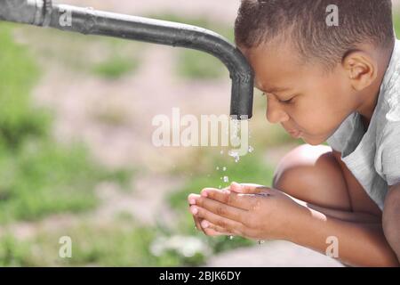 Afroamerikanisches Kind Trinkwasser aus dem Wasserhahn im Freien. Konzept der Wasserknappheit Stockfoto