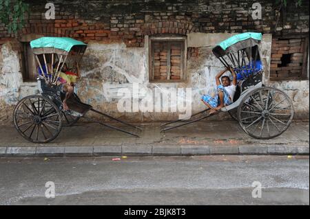 16.07.2011, Kolkata (Kalkutta), Westbengalen, Indien, Asien - zwei Rikscha-Abzieher ruhen auf ihren traditionellen alten Holzrickschas am Straßenrand. Stockfoto