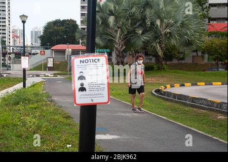 29.04.2020, Singapur, Republik Singapur, Asien - EINE Frau bedeckt ihr Gesicht mit einer schützenden Gesichtsmaske und geht an einer Notiz auf Covid-19 vorbei. Stockfoto