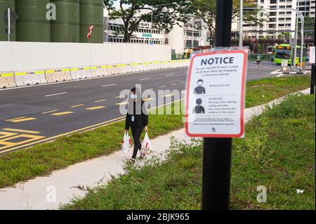 29.04.2020, Singapur, Republik Singapur, Asien - EINE Frau bedeckt ihr Gesicht mit einer schützenden Gesichtsmaske und geht an einer Notiz auf Covid-19 vorbei. Stockfoto