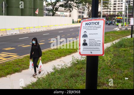 29.04.2020, Singapur, Republik Singapur, Asien - EINE Frau bedeckt ihr Gesicht mit einer schützenden Gesichtsmaske und geht an einer Notiz auf Covid-19 vorbei. Stockfoto