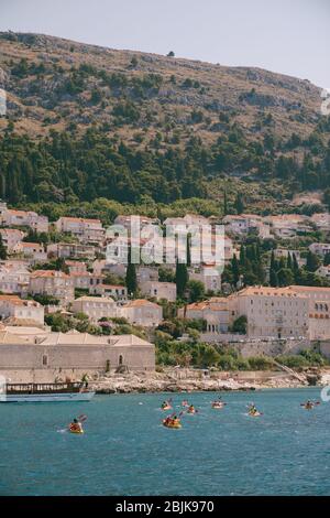 Eine Gruppe von Touristen reisen in Paaren Kajaks auf dem Meer vor der Kulisse eines Kreuzfahrtschiffes und der Küste, in der Nähe der Altstadt von Dubrovnik, Kroatien. Konzept Stockfoto