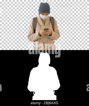 Frau in einem Mantel gekleidet, die medizinische Maske mit Telefon und Gehen, Alpha-Kanal Stockfoto