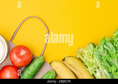 Papiertüte mit Lebensmitteln, Konserven, Tomaten, Gurken, Bananen, Salat auf gelbem Hintergrund. Spende, Quarantäne des Coronavirus. Lebensmittelbedarf für qu Stockfoto