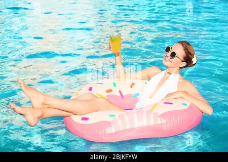 Schöne junge Frau mit einem Glas Cocktail entspannen auf aufblasbaren Donut im Pool Stockfoto