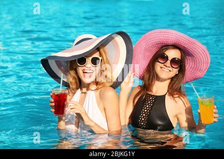 Zwei schöne Frauen mit Cocktails im Pool entspannen Stockfoto