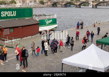 PRAG, TSCHECHISCHE REPUBLIK - 25. APRIL 2020: Menschen stehen in einer Schlange auf dem wiedereröffneten Naplavka Bauernmarkt, tragen Gesichtsmasken und halten Abstand Stockfoto