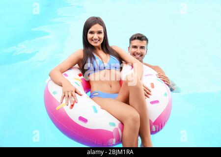 Junges Paar mit aufblasbarem Donut im Schwimmbad Stockfoto