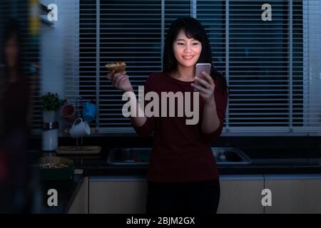 Asiatische Frau virtuelle Happy Hour Treffen und Essen Lieferung Pizza aus der Box online mit Freund oder Foto mit Handy-Kamera in der Küche Stockfoto