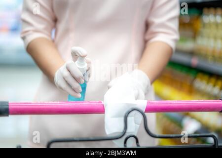 Hand der Frau mit Spritzen Alkohol antiseptische Desinfektion Spray Reinigung auf Warenkorb Wagen Griff Schutz während Coronavirus Pandemie Cov Stockfoto