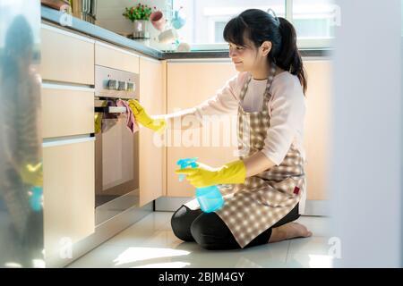 Asiatische Frau trägt Gummi Schutzhandschuhe Reinigung Backofen in ihrem Haus während des Aufenthalts zu Hause mit Freizeit über ihre tägliche Haushaltung Routine. Stockfoto