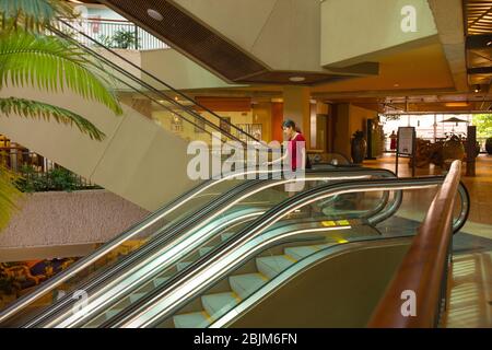 Biracial asiatische kaukasischen Teenager-Mädchen gehen Rolltreppe allein in leeren Waikiki Outdoor-Einkaufszentrum Stockfoto