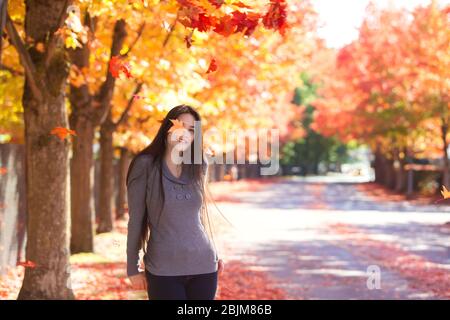 Biracial Teenager-Mädchen oder Frau unter fallenden Herbstblättern stehen, lächelnd Stockfoto