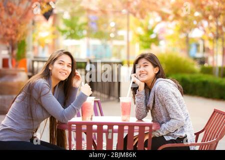 Zwei junge Mädchen oder Frauen sitzen zusammen und trinken im Café boba-Tee, lachen und lächeln Stockfoto