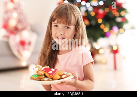 Nettes kleines Mädchen mit Plätzchen im Zimmer für Weihnachten dekoriert Stockfoto