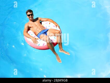 Junger Mann, der sich auf einem aufblasbaren Donut im Schwimmbad entspannt Stockfoto