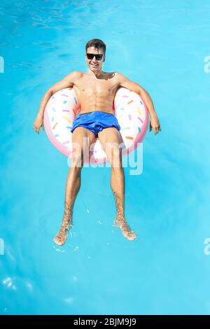 Junger Mann, der sich auf einem aufblasbaren Donut im Schwimmbad entspannt Stockfoto