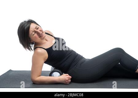 Eine Frau mittleren Alters, auf einer Gymnastikmatte mit myofaszialer Walze, hat Rückenschmerzen, auf weißem Hintergrund. Stockfoto