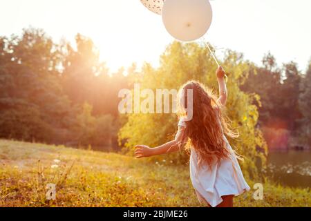 Hübsches kleines Mädchen, das mit Ballonen in der Hand läuft. Kind mit Spaß im Sommerpark. Aktivitäten im Freien Stockfoto