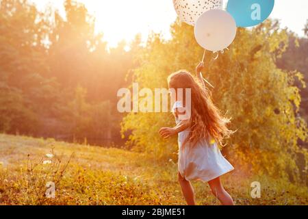 Hübsches kleines Mädchen, das mit Ballonen in der Hand läuft. Kind mit Spaß im Sommerpark. Aktivitäten im Freien Stockfoto