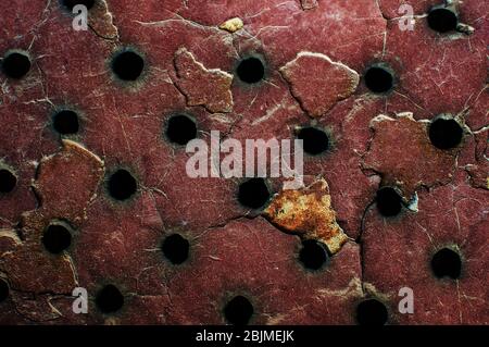 Roter Metallhintergrund mit schwarzen Löchern, Rost und Abrieb. Alte Eisentür in der Garage. Kopierbereich. Stockfoto