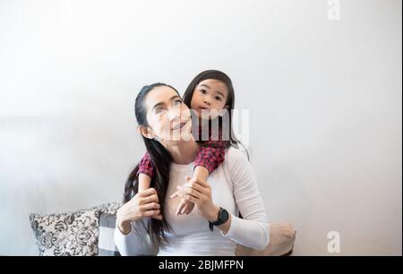 Die Tochter umarmt und spielt mit ihrer Mutter und lacht und lächelt glücklich auf dem Sofa, während sie sich zu Hause entspannt. Stockfoto