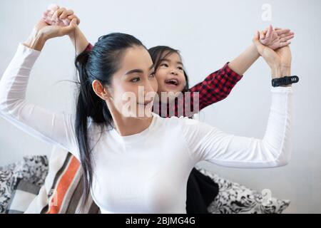 Die Tochter umarmt und spielt mit ihrer Mutter und lacht und lächelt glücklich auf dem Sofa, während sie sich zu Hause entspannt. Stockfoto