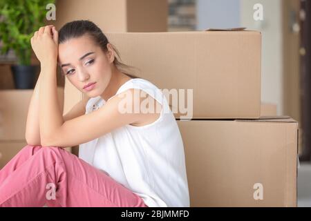 Müde junge Frau sitzt auf dem Boden in ihrer neuen Wohnung in der Nähe von Umzugsboxen Stockfoto