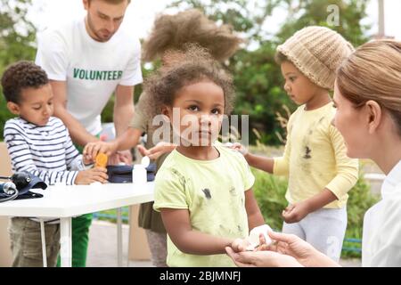 Freiwillige geben Vitamintabletten an arme afrikanische Kinder im Freien Stockfoto