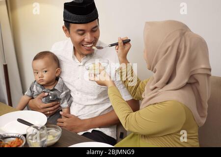 Schöne Hijab-Frau, die ihrem Mann etwas Essen serviert, während sie abends das Fasten brach Stockfoto