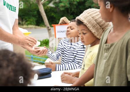 Freiwillige geben Vitamintabletten an arme afrikanische Kinder im Freien Stockfoto