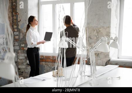 Details. Weibliche Maklerin zeigt einem jungen Mann nach einer Diskussion über die Baupläne ein neues Zuhause. Die Wahl der Baustoffe, Reparatur, Technologien in Smart House. Umzug, neues Home-Konzept. Stockfoto