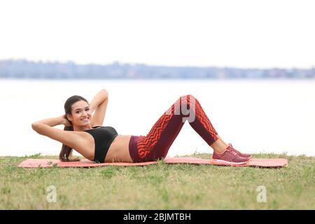 Junge sportliche Frau macht Bewegung am Ufer des Flusses Stockfoto