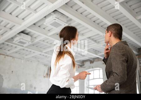 Zukunft. Weibliche Maklerin zeigt einem jungen Mann nach einer Diskussion über die Baupläne ein neues Zuhause. Die Wahl der Baustoffe, Reparatur, Technologien in Smart House. Umzug, neues Home-Konzept. Stockfoto