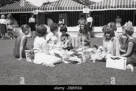 1964, historisch, eine Gruppe von neuen weiblichen Studenten an der Erstsemester Woche sitzen auf dem Gras draußen mit Mittagessen zusammen, Kalifornien, USA, in einem Bild, das die Mode und Frisuren der jungen College-Frau in dieser Ära zeigt. Stockfoto