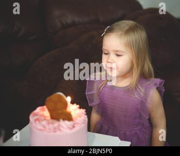 Kleines Mädchen in Lavendel Kleid bereitet sich auf die Luft blasen Kerzen auf einem Urlaub Kuchen. Stockfoto