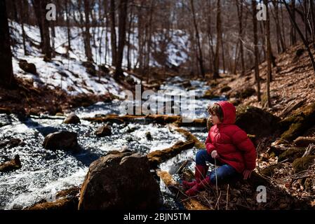 Junge sitzt an einem gefrorenen See im frühen Frühjahr, USA Stockfoto