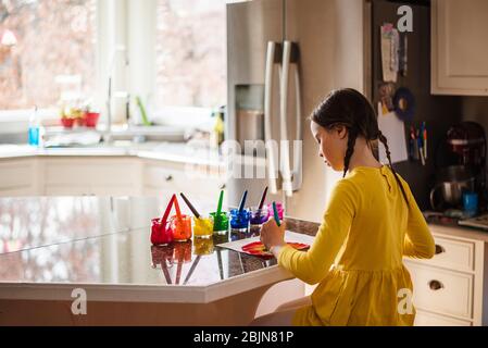 Mädchen sitzt in der Küche Malerei einen Regenbogen Stockfoto