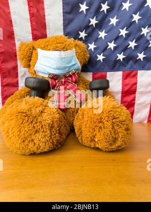 Teddybär mit Gesichtsmaske und Kurzhanteln. Flagge der USA Stockfoto