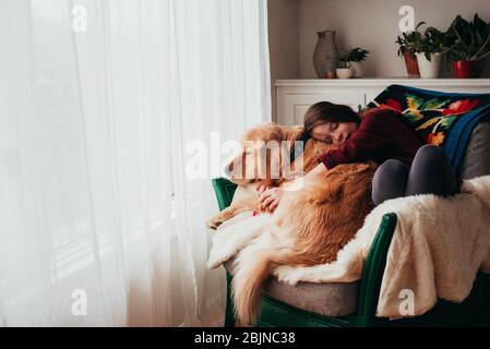 Mädchen sitzt in einem Sessel und kuschelt ihren Hund Stockfoto