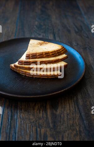 Würzige Scheiben aus geräuchertem Käse aus dem Terkassischen Dreieck auf dunklem Holzteller mit Gewürzen. Bereit zum Essen. Stockfoto