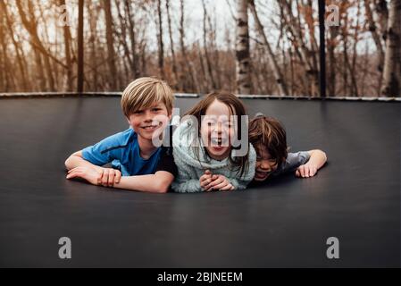 Drei lächelnde Kinder liegen auf einem Trampolin im Garten, USA Stockfoto