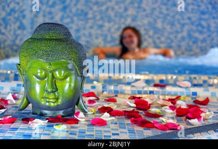 Buddha Kopf und Rosenblätter in einem Spa, junge Frau in einem Whirl-Pool im Hintergrund, Frankreich, Savoie, Sainte-Foy-Tarentaise Stockfoto