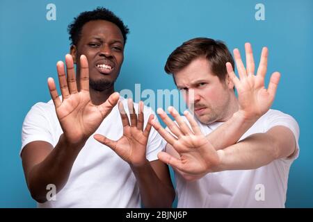 Zwei Männer afroamerikanischen und kaukasischen machen Stop-Zeichen machen eine soziale Distanz oder Ablehnung Geste. Studioaufnahme Stockfoto