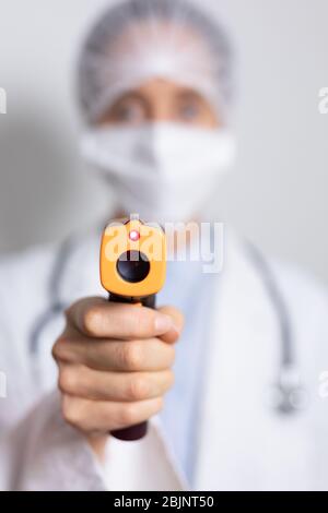 Medizinisches Personal hält Pistolenthermometer und trägt Coronavirus Covid19 Maske Stockfoto