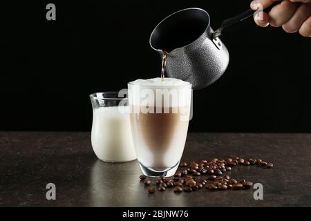 Person, die Latte Macchiato auf schwarzem Hintergrund macht Stockfoto