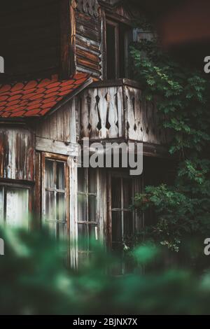Vertikale Aufnahme mit einer flachen Schärfentiefe einer hölzernen verblassten Fassade eines alten gemütlichen zweistöckigen Sommerhauses mit Balkon Stockfoto