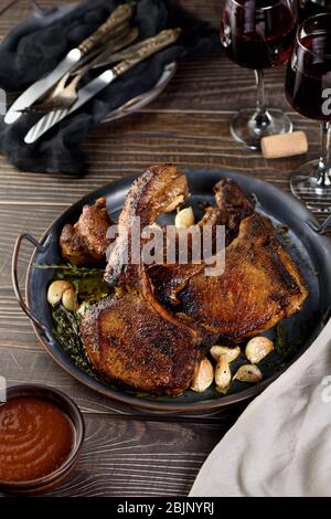 Saftig, Scheibe gebratenes Schweinefleisch auf einem Knochen in Öl mit Knoblauch und Kräutern in einer Pfanne. Stockfoto