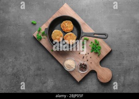 Holzbrett mit Lachs-Patties in der Pfanne auf dem Tisch Stockfoto