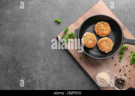 Holzbrett mit Lachs-Patties in der Pfanne auf dem Tisch Stockfoto